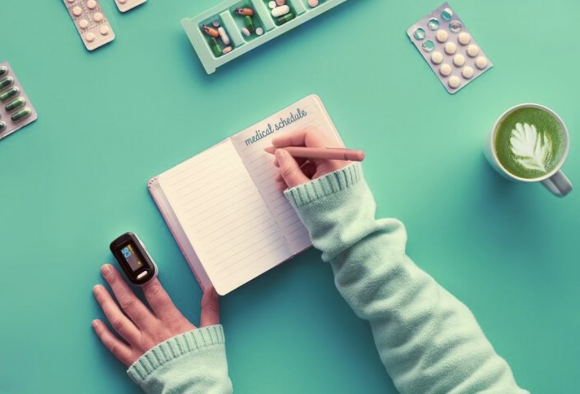 Запись медицинского расписания, пульсоксиметр, органайзер для таблеток и чашка напитка на мятном фоне